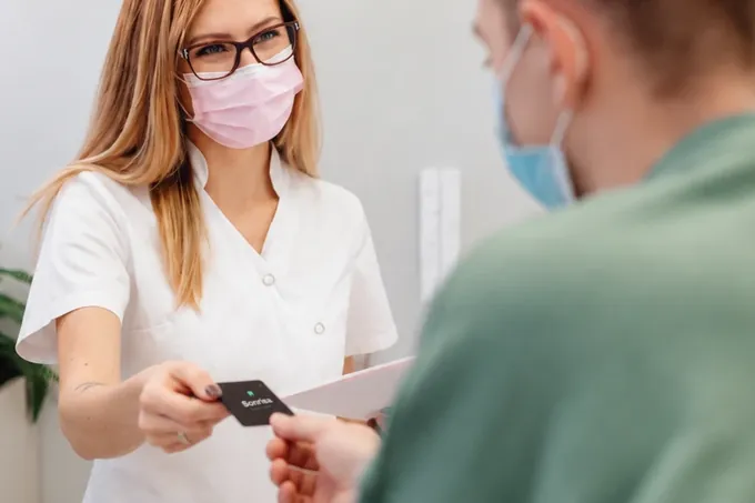 En la recepción de una clínica dental, la recepcionista le entrega al paciente su NOIR card de Sonrisa