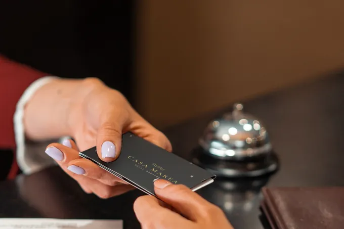 En la recepción de un hotel, la recepcionista entrega la NOIR card de Casa Marea al huésped