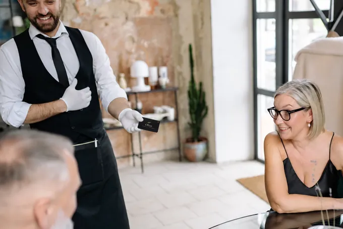 En un restaurante, el mesero le entrega a la mesa la NOIR card de Olivo